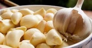 A white bowl filled with peeled garlic cloves and a whole garlic bulb.